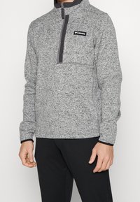 Pullover in fleece grigio a fantasia con mezza zip, colletto alto e tasca sul petto. Presenta finiture nere e un piccolo logo sul davanti.