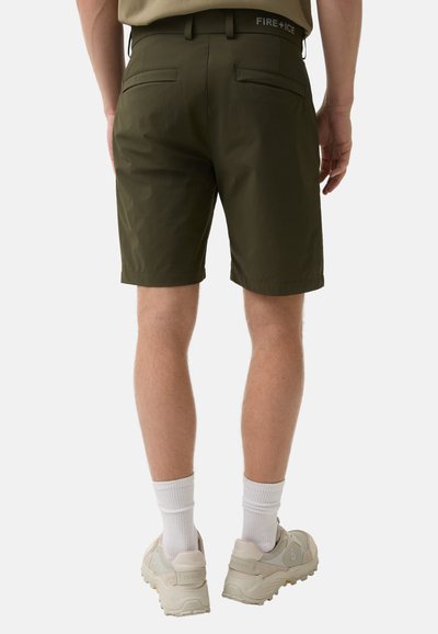 Dunkelgrüne Shorts mit glatter Textur, Gesäßtaschen und einem kontrastierenden Logo am Bund. Kombiniert mit weißen Socken und hellen Schuhen.