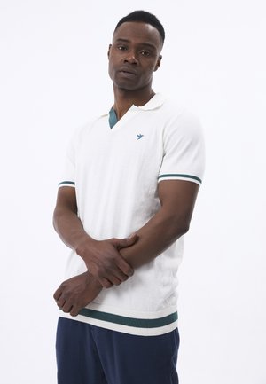 Polo-shirt en tricot blanc avec un accent vert sur le col et les manches. Présente un logo sur la poitrine et un tissu texturé.