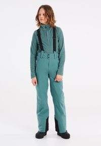 Pantalons de ski teal avec bretelles noires réglables, taille haute et coupe élégante. Comprend des poches zippées et des panneaux de cheville noirs renforcés.