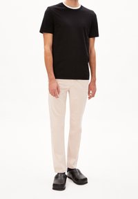 Černé tričko s krátkými rukávy a bílým límcem, v kombinaci se světle béžovými kalhotami a černými dřeváky, zobrazené na neutrálním pozadí.