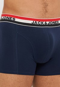 Boxer shorts bleu marine avec une texture douce, arborant une ceinture élastique contrastante en rouge, blanc et noir avec le logo "JACK & JONES".