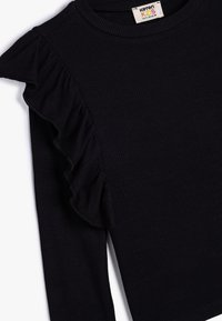 Haut noir à manches longues côtelé avec une accent ruffle sur l'épaule gauche, un col rond et une texture de tissu douce.