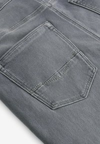 Țesătura de denim gri, cu un buzunar din spate cu un design în formă de vânare și detalii de cusătură contrastante, textură netedă și ușor lucioasă.