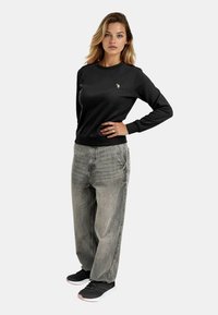 Black sweatshirt with crew neck and ribbed hem, paired with light gray baggy jeans and black sneakers, featuring a small logo on the chest.