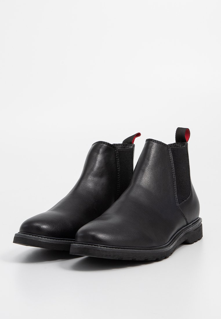Bottines noires en cuir avec panneaux élastiques sur les côtés, bout rond, petit talon, et tirant rouge. Tige texturée avec une finition lisse.