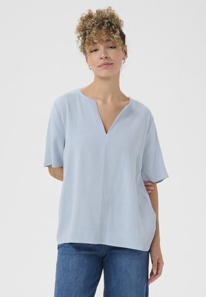 Lichtblauwe blouse met korte mouwen en V-hals, ontspannende pasvorm en een zachte textuur. Draag met blauwe spijkerbroeken. Eenvoudig, strak ontwerp.