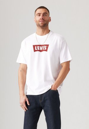 Bílý bavlněný tričko s červeným logem Levi's. Krátké rukávy, design s kulatým výstřihem, v kombinaci s tmavě modrými džíny pro kontrast.