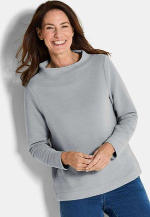 Pull en tricot gris texturé avec un col cheminée haut, des manches longues et une coupe décontractée. Porté sur un jean bleu.