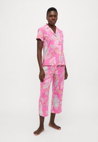 Rozā pidžamu komplekts, kas sastāv no īsām piedurknēm, pogājama krekla un īsām biksēm. Dizainā ietilpst krāsaini peļļu raksti uz viegla auduma.