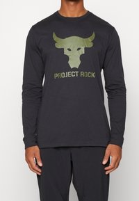 Mann trägt ein schwarzes Langarmshirt mit einem grünen Büffelkopf-Logo und dem Text "PROJECT ROCK" auf der Vorderseite.