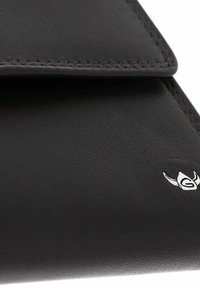 Gros plan sur un coin d'un portefeuille en cuir noir avec des coutures visibles et un petit emblème argenté en bas à droite.