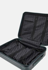Hartschalenkoffer in Dunkelgrün mit schwarzem Innenraum. Verfügt über mehrere Fächer, Netzsteckfächer und Reißverschlussverschlüsse.
