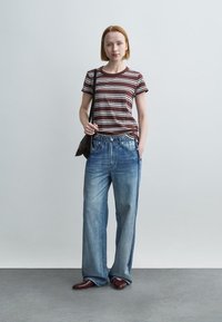 Ριγέ μπλουζάκι σε καφέ και κρεμ, συνδυασμένο με ανοιχτό μπλε φαρδιά τζιν παντελόνια με ρίγες στο πλάι. Καφέ δερμάτινα παπούτσια και τσάντα ώμου.