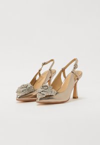 Tacones slingback de punta fina en oro rosado, con un detalle floral texturizado adornado con rhinestones y un tacón de aguja de altura media.