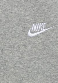Grå sweatshirt i mjukt tyg, med en liten vit broderad Nike-logotyp på framsidan, med en jämn och slät yta.