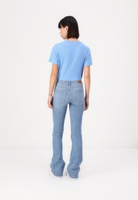 Light blue t-shirt with short sleeves, paired with light wash flared jeans, featuring back pockets and a brown leather label on the waistband.