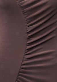 Κοντινό πλάνο καφέ υφάσματος με λείες και ριγωτές υφές ραμμένες μαζί σε καμπυλωτή ραφή.