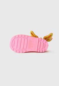 Semelle de chaussure en caoutchouc rose avec une texture antidérapante et des accents en forme de papillon jaunes et orange le long du talon. Profil plat, construction légère.
