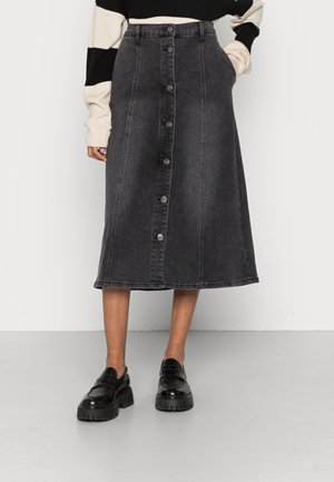 Sort midi-jeansnederdel med knapper foran, båret med sorte chunky loafers og en sort-hvid langærmet sweater.