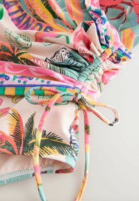 Tela multicolorida con un patrón tropical que presenta hojas, tigres y cangrejos. Secciones fruncidas con lazos ajustables en colores vibrantes.