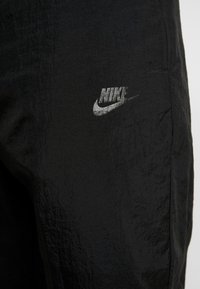 Svart texturerad tyg med en grå Nike-logotyp och swoosh på övre lårområdet av byxorna.