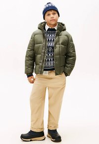 Green puffer jacket with a hood, blue patterned knit sweater, beige pants, and black footwear with beige soles. Casual winter outfit.