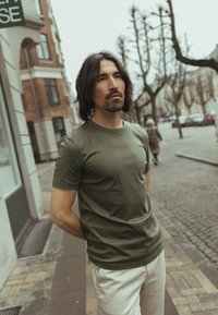 Olijfgroen, kortarmig T-shirt van gladde stof, gecombineerd met lichtgekleurde broek. Eenvoudig ontwerp zonder zichtbare patronen of accenten.