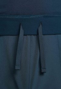 Ceinture élastique bleu marine avec deux cordons plats sur tissu bleu foncé, montrant des coutures détaillées et une texture.