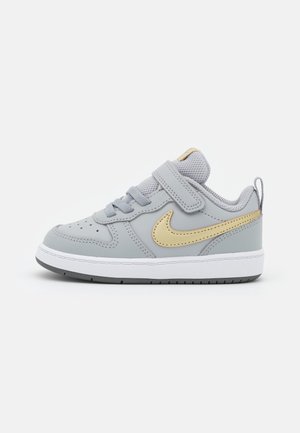 Grå småbørns sneakers med gylden Nike-swoosh, hvid sål, snørebånd og velcrolukning på en ensartet hvid baggrund.