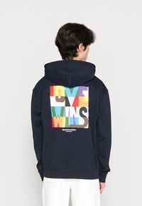 Sudadera azul marino con un gráfico multicolor que incluye el texto "LOVE WINS" y un logo en la parte inferior. Tejido suave y corte relajado.