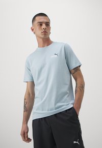 Camiseta de algodón azul claro con mangas cortas, con un pequeño logo blanco de "PUMA" y un logo de gato negro en el pecho.