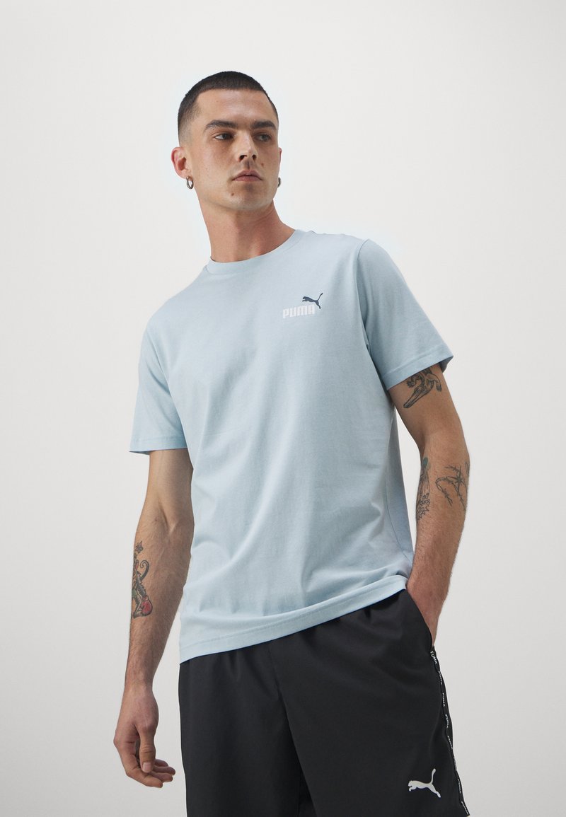 Camiseta de algodón azul claro con mangas cortas, con un pequeño logo blanco de "PUMA" y un logo de gato negro en el pecho.