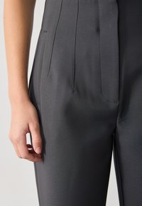 Maßgeschneiderte graue Hose aus glattem Stoff mit Vorderentaschen, dezenten Falten und einer figurschmeichelnden Silhouette.