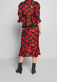 Schwarzes Kleid und Jacken-Set mit Blumenmuster, das rote Mohnblumen, Rüschensäume und einen ausgestellten Saum beinhaltet. Betont durch Aussparungen.