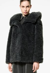 Cappotto corto in peluche nero con ampio colletto, esterno testurizzato e chiusura con zip, caratterizzato da una vestibilità larga e maniche lunghe.