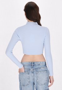 Top corto a maniche lunghe di colore blu chiaro a coste con collo alto, abbinato a jeans blu chiaro a vita alta con tasche posteriori visibili.