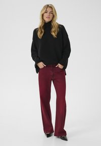 Crna turtleneck(puli) majica s rebrastim rukavima, uparena s uskim burgundskim trapericama i crnim cipelama s oštrim vrhom na jednostavnoj bijeloj pozadini.