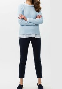 Světle modrý pletený svetr s kulatým výstřihem, přes bílou pruhovanou košili s límečkem, kombinovaný s tmavě námořnickými slim-fit kalhotami a tmavými botami.