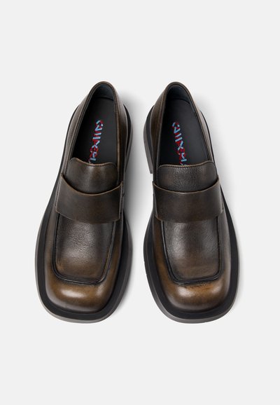 Brown leather shoes with a rectangular toe shape, a front strap, and a thick black sole. Textured surface with subtle color variations.