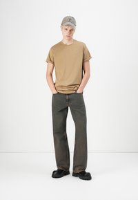 Beige katoenen t-shirt, relaxed fit, gecombineerd met slate grijze denim jeans, losse stijl met zichtbare stiksels, aangevuld met zwarte chunky schoenen.