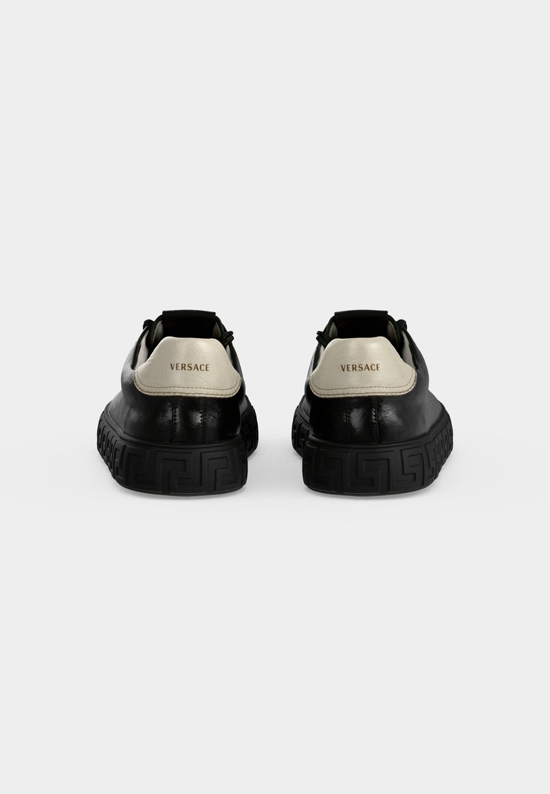Paar schwarze Leder-Versace-Sneakers mit weißen Fersenlaschen und geprägten gemusterten schwarzen Sohlen, von hinten vor weißem Hintergrund gezeigt.