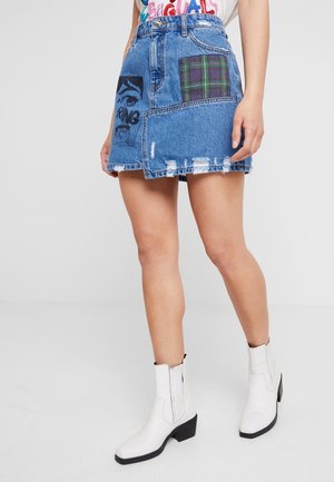 Jeansowa spódnica z postrzępionymi brzegami, wieloma wzorzystymi łatami w odcieniach niebieskiego i kratki, dopasowana w talii, z lekko rozkloszowanym dołem. Noszona z białymi botkami za kostkę.