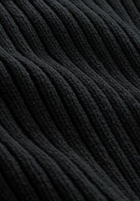 Gros plan sur un tissu noir tricoté montrant une texture côtelée verticale épaisse et un fil doux légèrement duveteux.