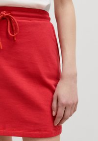 Rode katoenen mix rok met een geribbelde elastische tailleband, verstelbare trekkoord en een zachte textuur. De zoomlijn zit boven de knie.