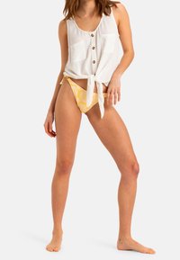 White sleeveless top with buttons and a tied front, paired with yellow bikini bottoms featuring a floral pattern.