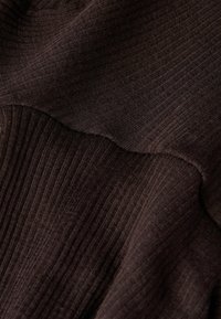 Tmavě hnědá tkanina s vroubkovanou texturou a hladkými křivkami. Materiál se zdá být měkký s různými vzory na povrchu.