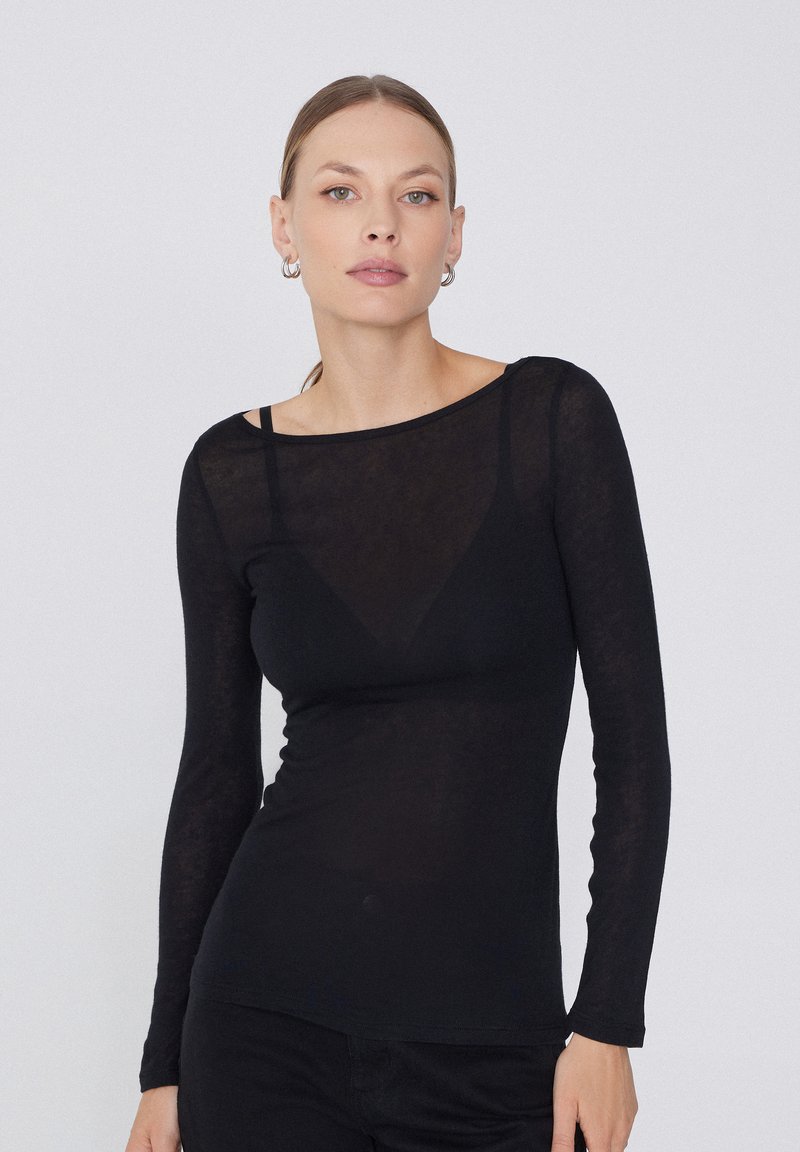 Haut noir à manches longues en tissu transparent, doté d'un col bateau et d'une silhouette ajustée. Texture subtile avec transparence sur la partie supérieure du corps.