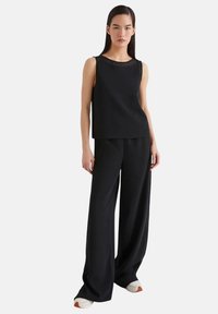 Top nero senza maniche e pantaloni a vita alta a gamba larga, realizzati in tessuto morbido. L'outfit presenta un design semplice e una vestibilità comoda.