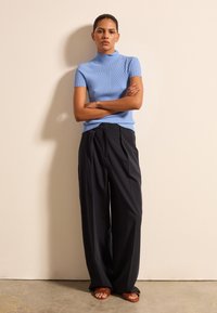 Hellblaues, geripptes Kurzarmoberteil kombiniert mit weiten schwarzen Hosen und braunen geflochtenen Sandalen. Einfaches, tailliertes Design mit subtiler Textur.